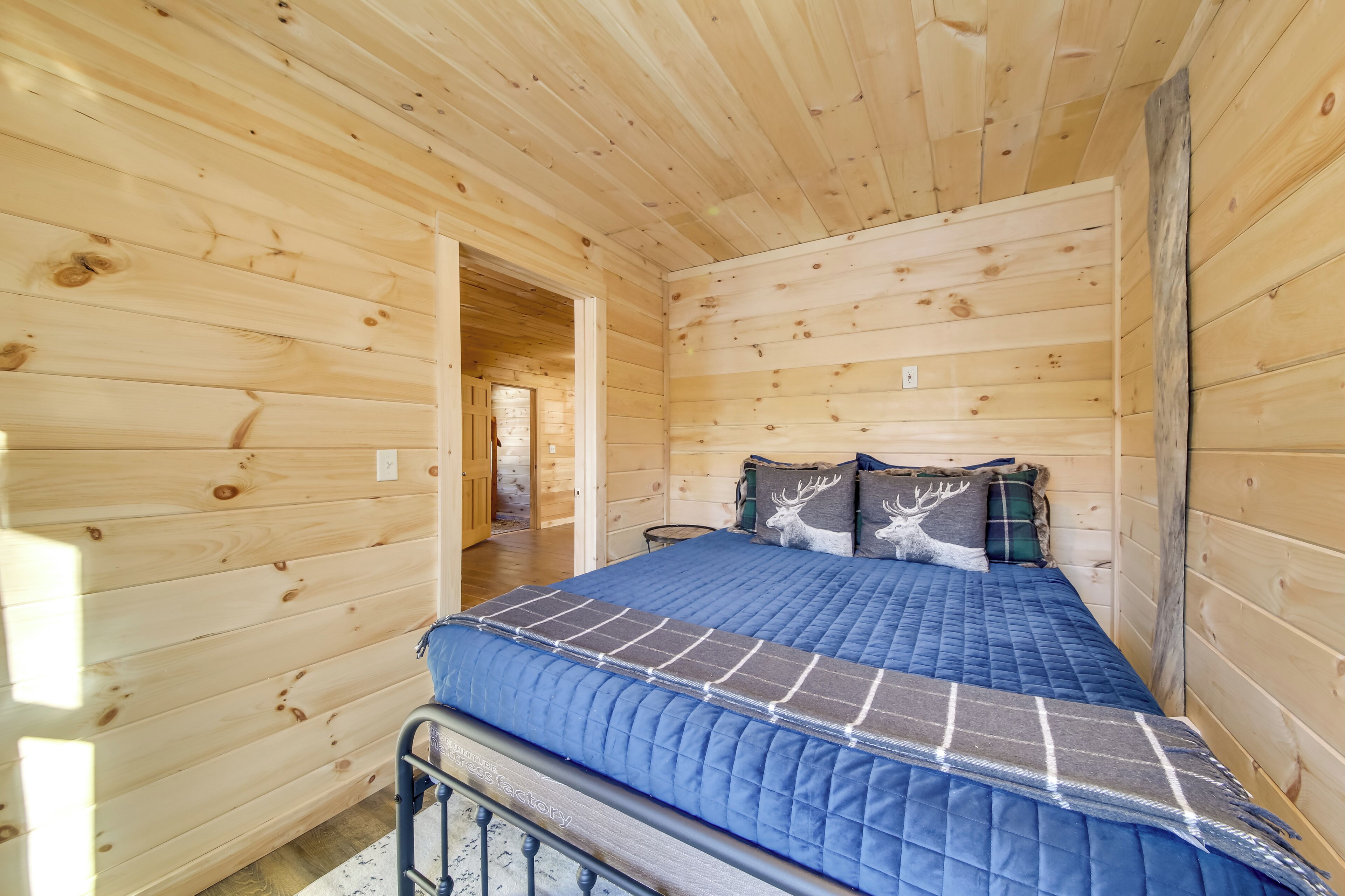 A wooden cabin room with a bed, a nightstand, and a door leading to another room.