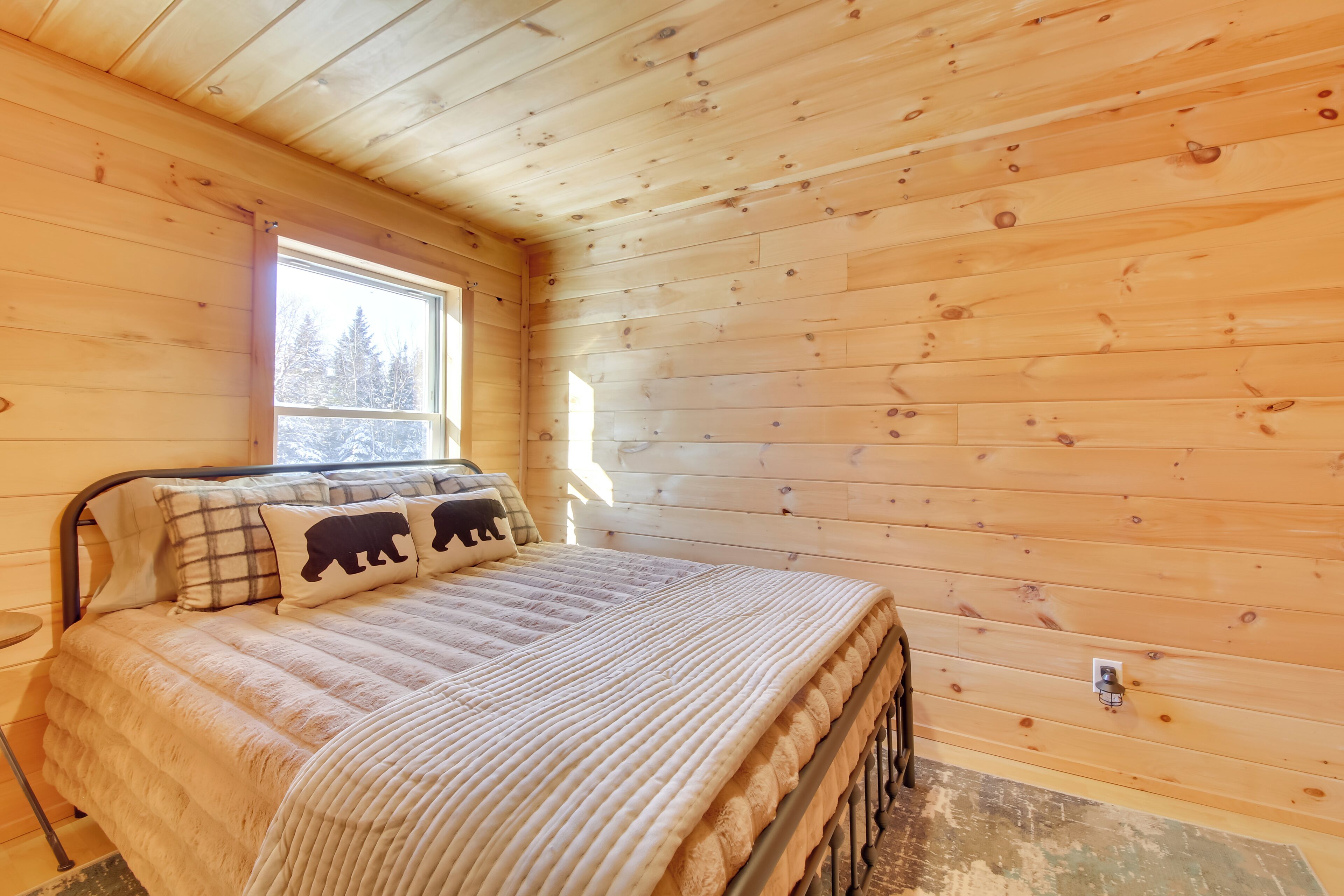 A wooden cabin bedroom with a bed, a window, and a door.