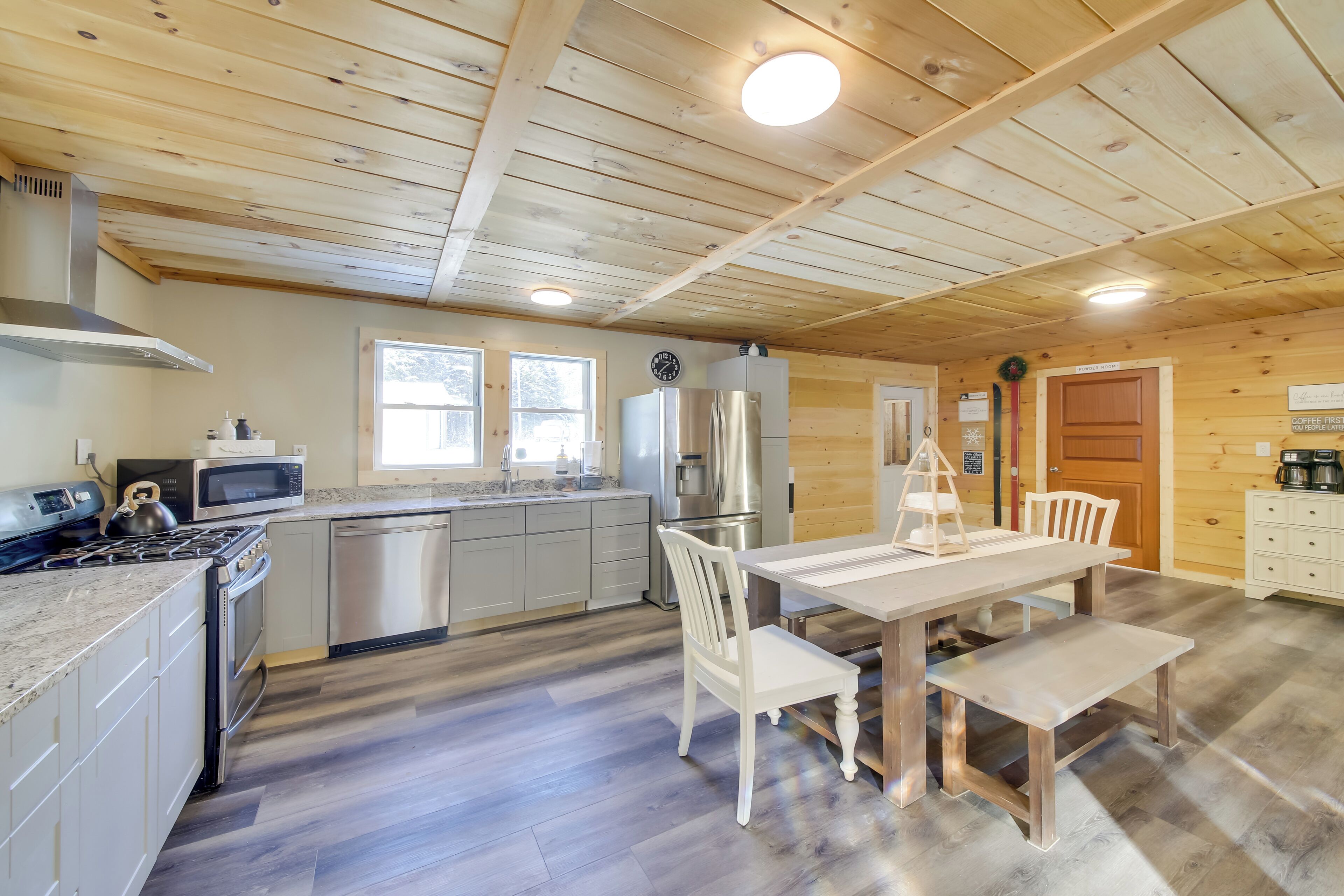A modern kitchen with stainless steel appliances, a wooden ceiling, and a dining area with a white table and chairs.