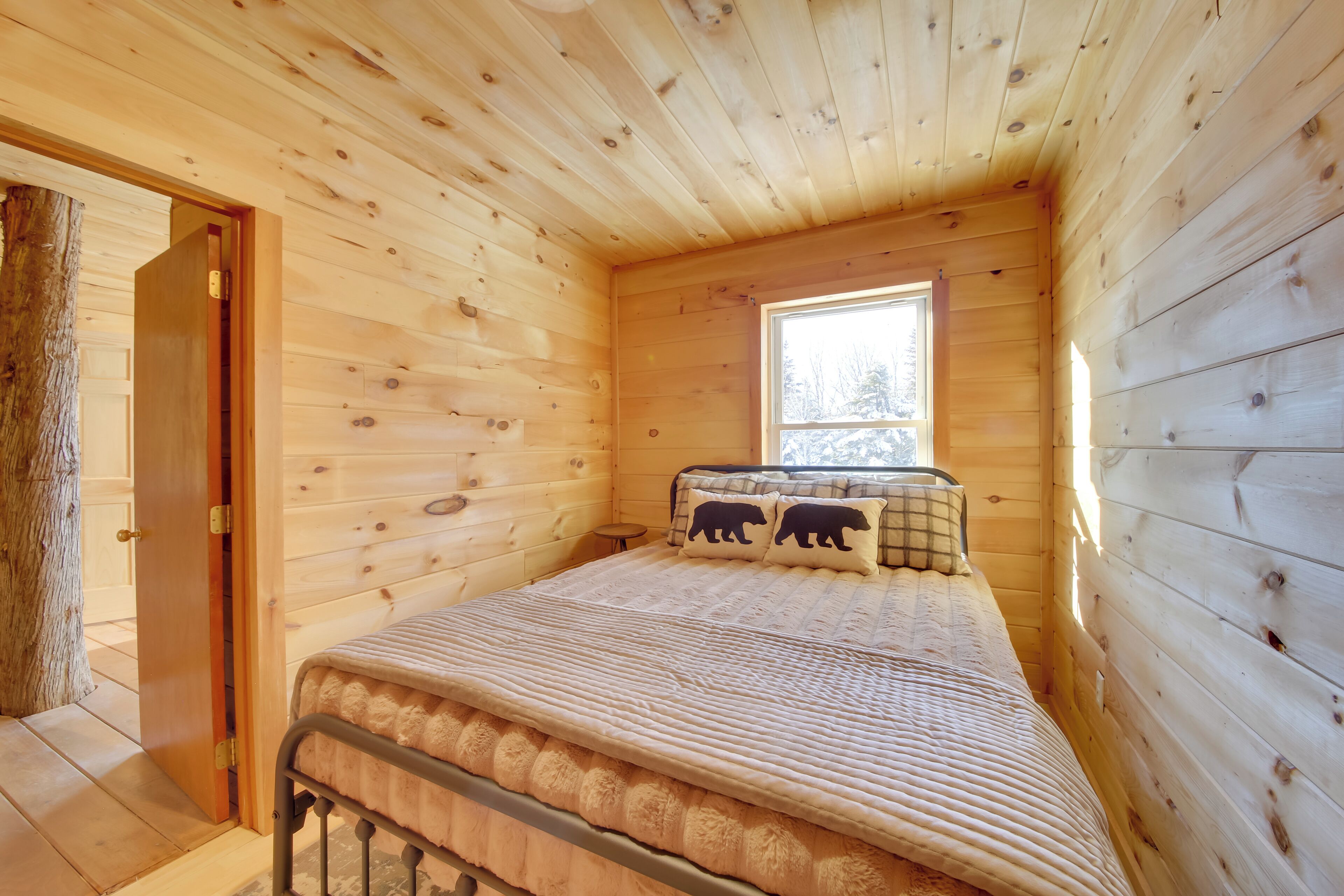 Un dormitorio de cabaña de madera con cama, ventana y puerta.