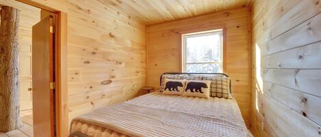 Un dormitorio de cabaña de madera con cama, ventana y puerta.