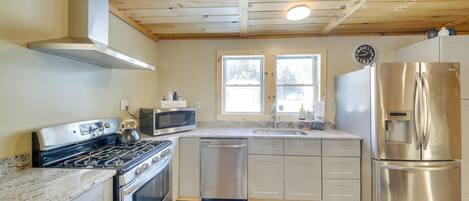 A modern kitchen with stainless steel appliances, wooden ceiling, and a window providing natural light.