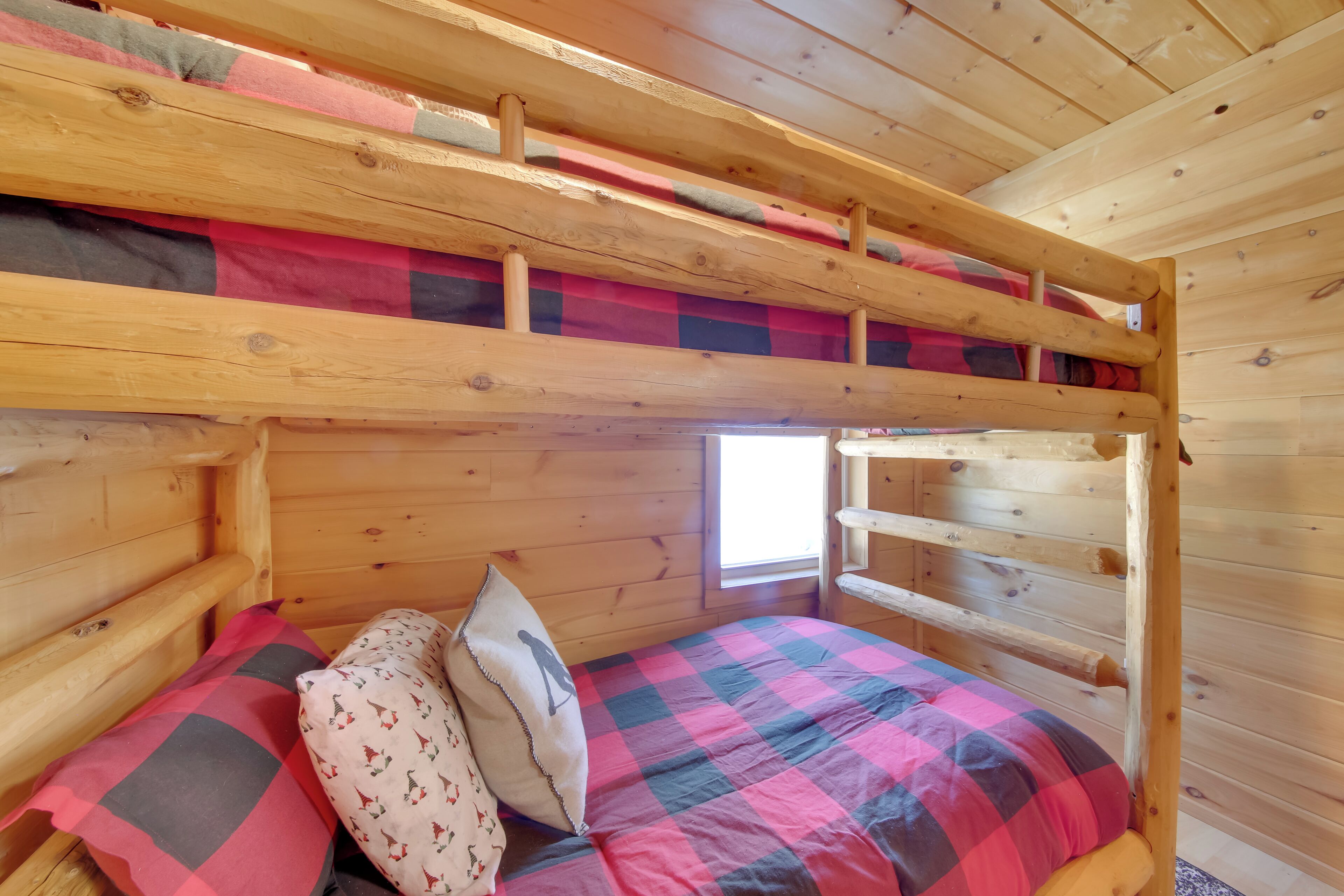Ein Stockbett mit karierter Bettdecke und Kissen, Holzwände und ein kleines Fenster.