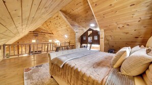 Camera da letto in una baita di legno con zona notte soppalcata, un letto con coperta trapuntata e una ringhiera in legno che si affaccia sul balcone.