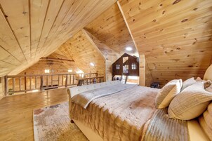 Dormitorio de cabaña de madera con un entrepiso para dormir, una cama con manta acolchada y barandilla de madera con vistas al balcón.