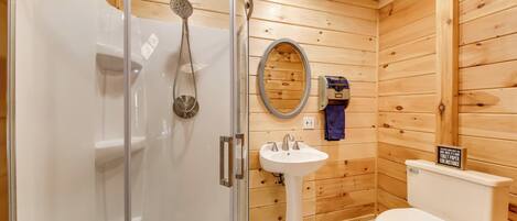 Baño de cabaña de madera con mampara de vidrio, lavabo pedestal, inodoro y pared de madera.