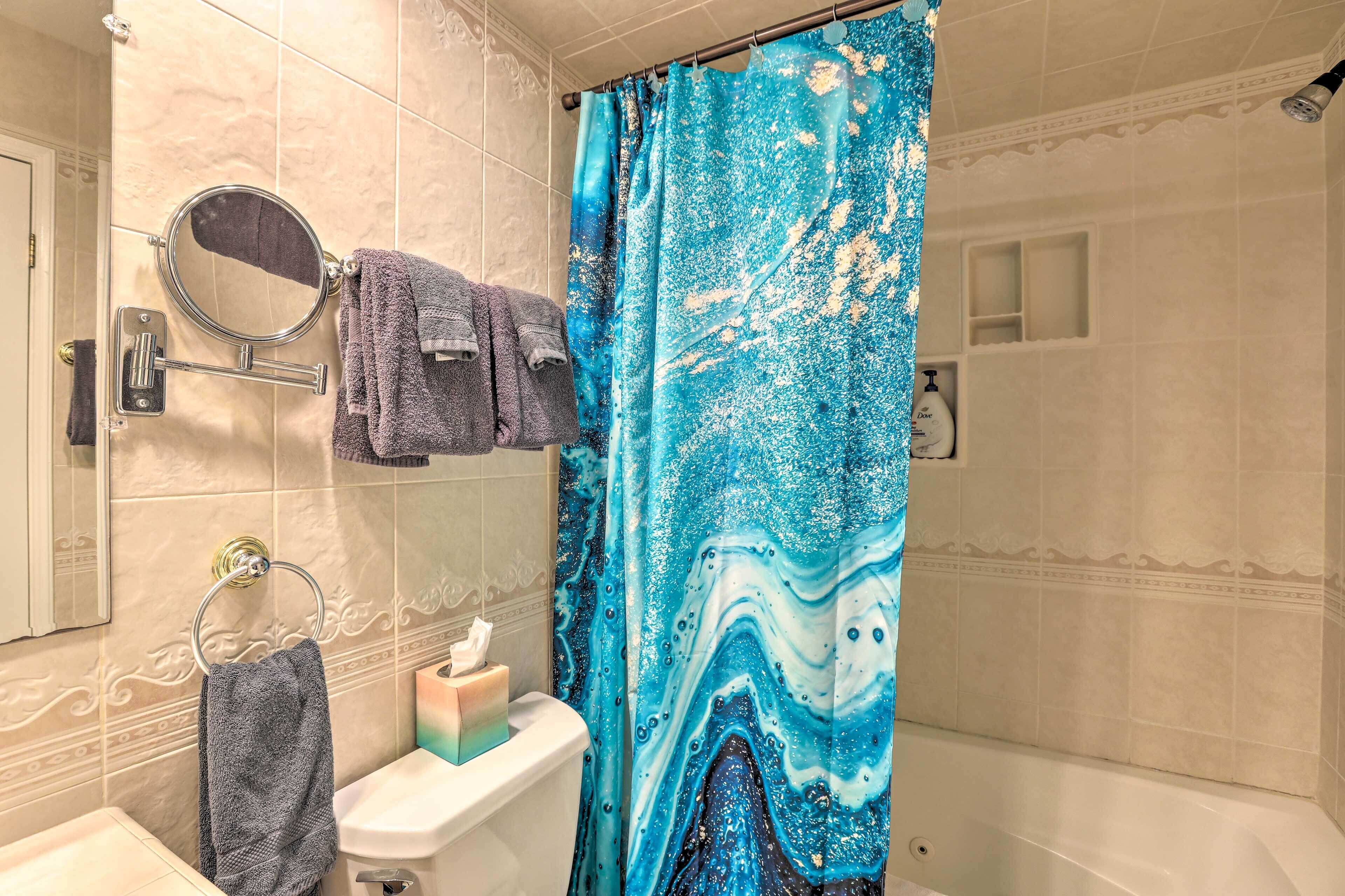 A bathroom with a blue shower curtain, a sink with a soap dispenser, and a towel rack with multiple towels.