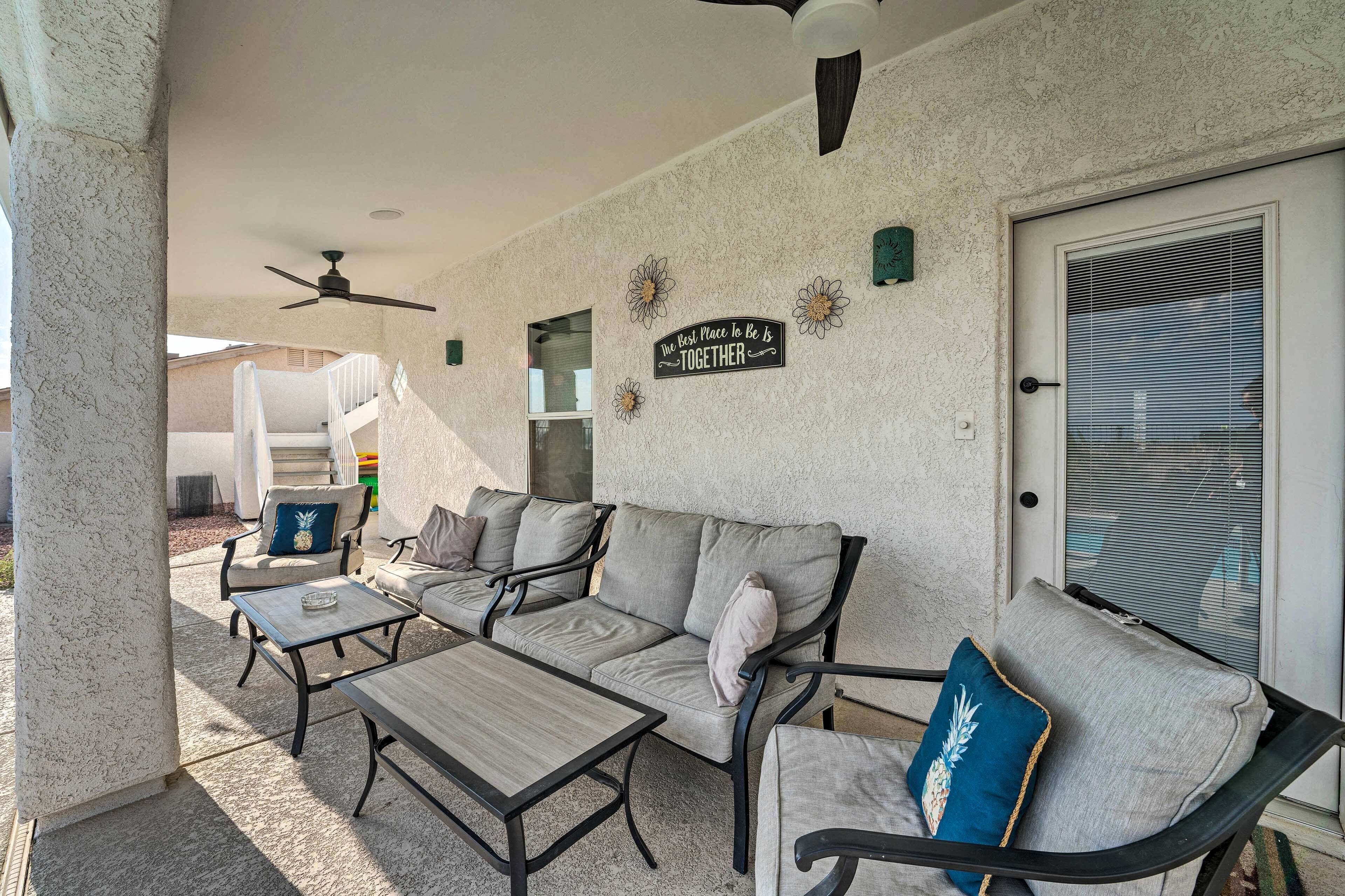 A covered patio area with a sofa, two tables, and a ceiling fan.