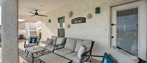 A covered patio area with a sofa, two tables, and a ceiling fan.