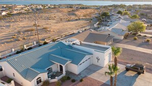 A residential area with houses featuring blue-tiled roofs and white walls, surrounded by dry terrain and a body of water in the background. - Pool, Patio & Lake Views: Lake Havasu City Home! (Lake Havasu City)