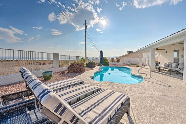 A backyard with a swimming pool, lounge chairs, and a covered patio area.