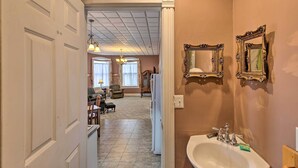 Un baño con lavamanos, espejo y puerta que da a una sala de estar con candelabro.
