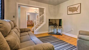 A living room with a sectional sofa, a flat-screen TV, a chandelier, and a framed map of the USA on the wall. - Blue Ridge Mountains Cottage w/ Pergola & Fire Pit (Hendersonville)