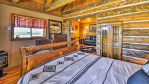 A log cabin bedroom with a wooden bed, a dresser, and a window with plaid curtains.