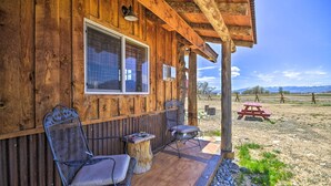 A wooden cabin with a porch, two chairs, a table, and a picnic table in the background.