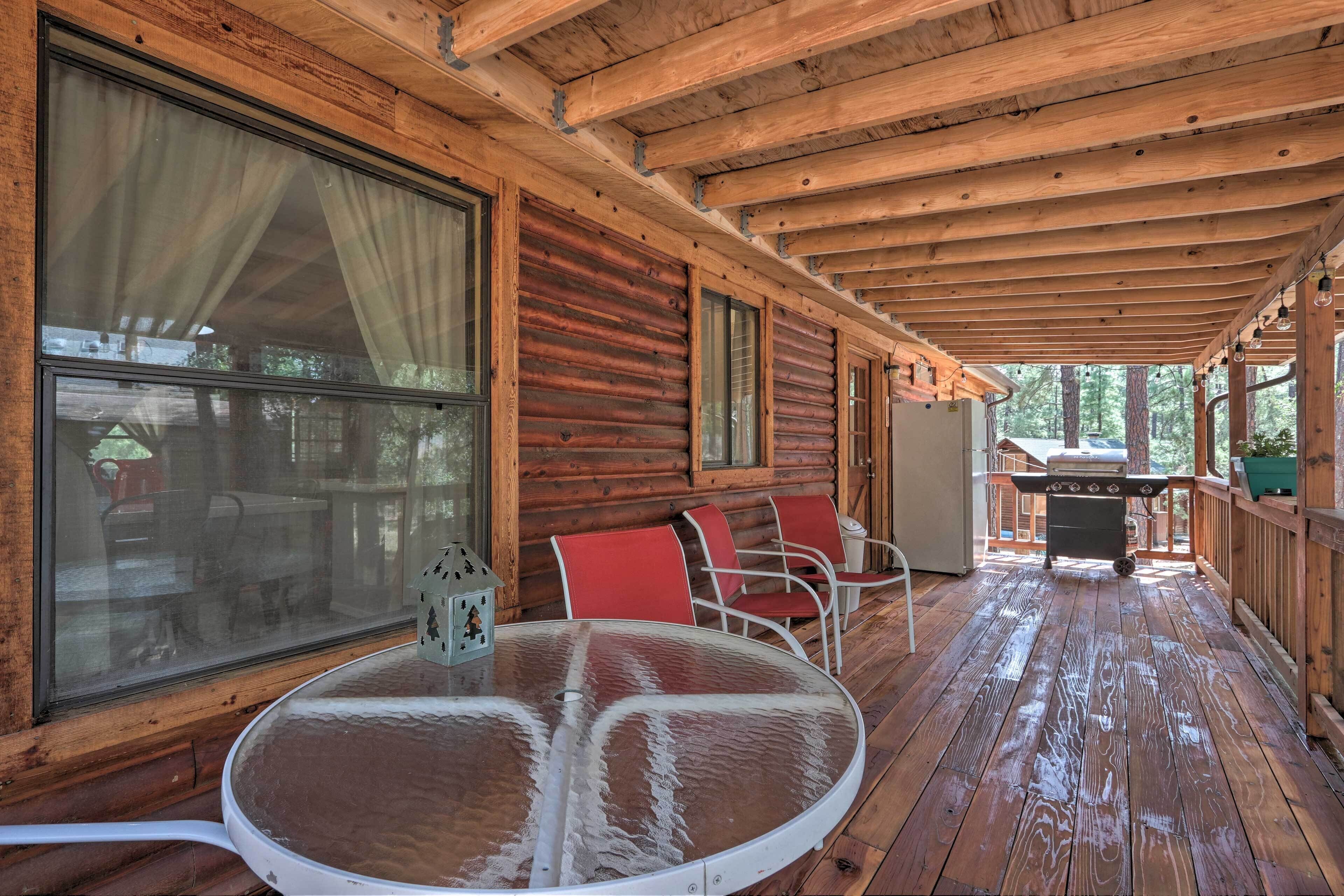 A wooden deck with a round table and chairs, a grill, and large windows with curtains.