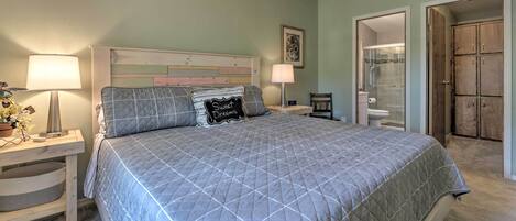 A bedroom with a bed, nightstands, a lamp, a wall art piece, and a door leading to a bathroom.