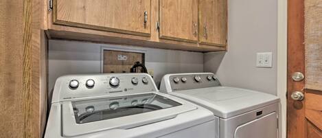 A laundry room with two white Maytag washers and dryers, wooden cabinets above, and a door with a textured mat.