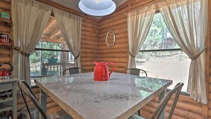 Eine Holzhütte mit Esstisch, Stühlen, einer roten Karaffe und Vorhängen.