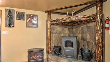 A stone fireplace with a modern wood-burning stove, a small heater, and a bucket.
