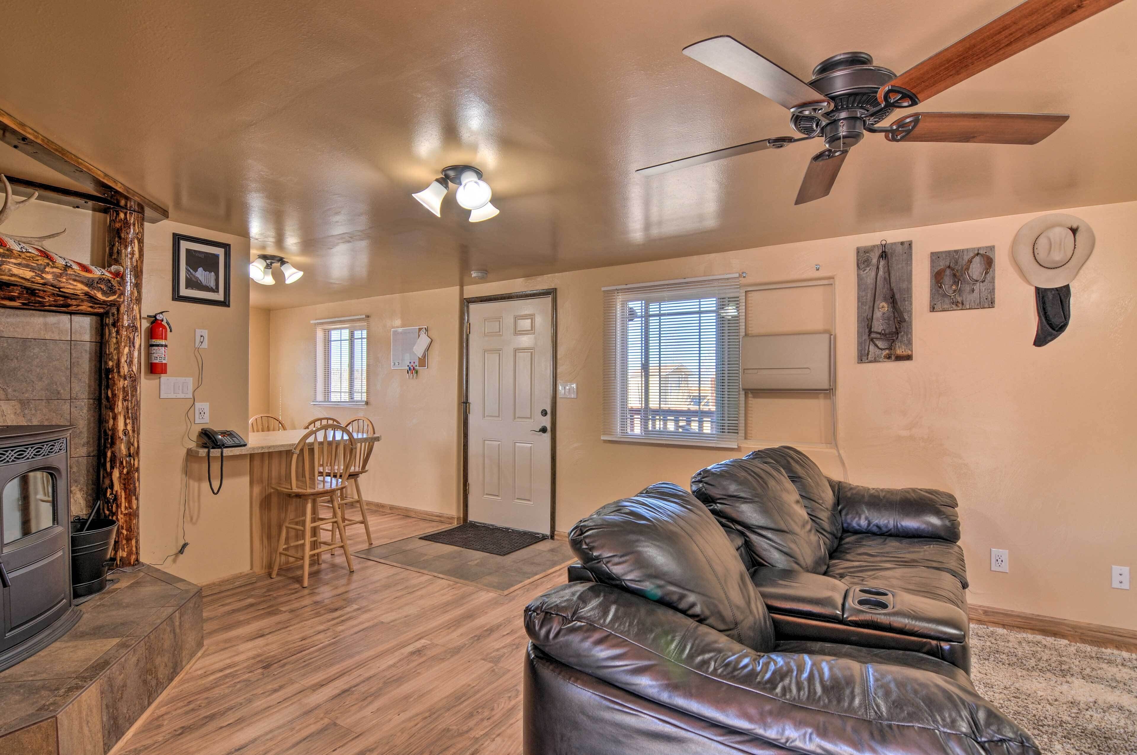 A living room with a leather couch, a dining area with a table and chairs, a fireplace, and a ceiling fan.