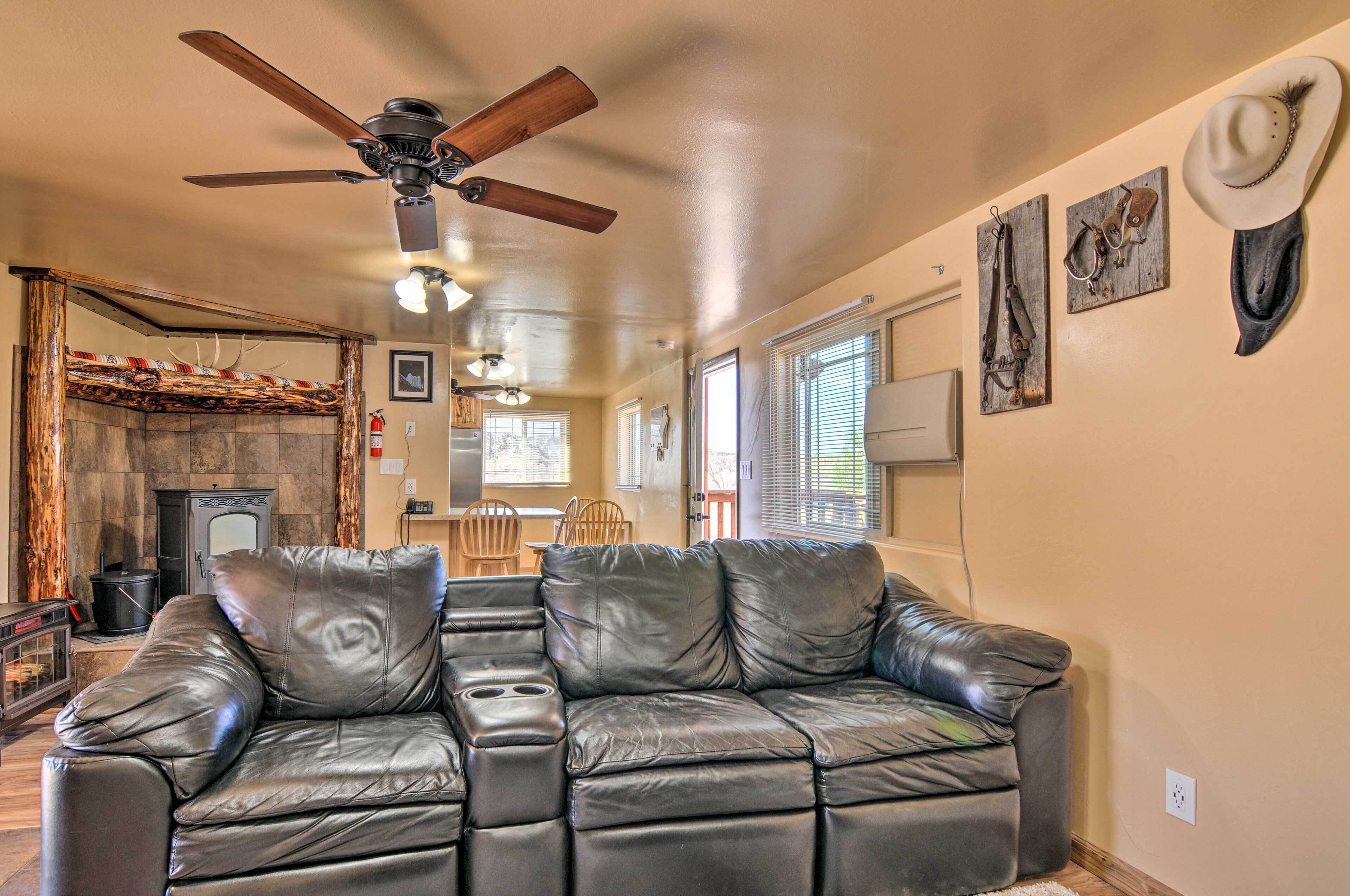 A living room with a leather sectional sofa, a ceiling fan, a fireplace, and wall-mounted cowboy hats.