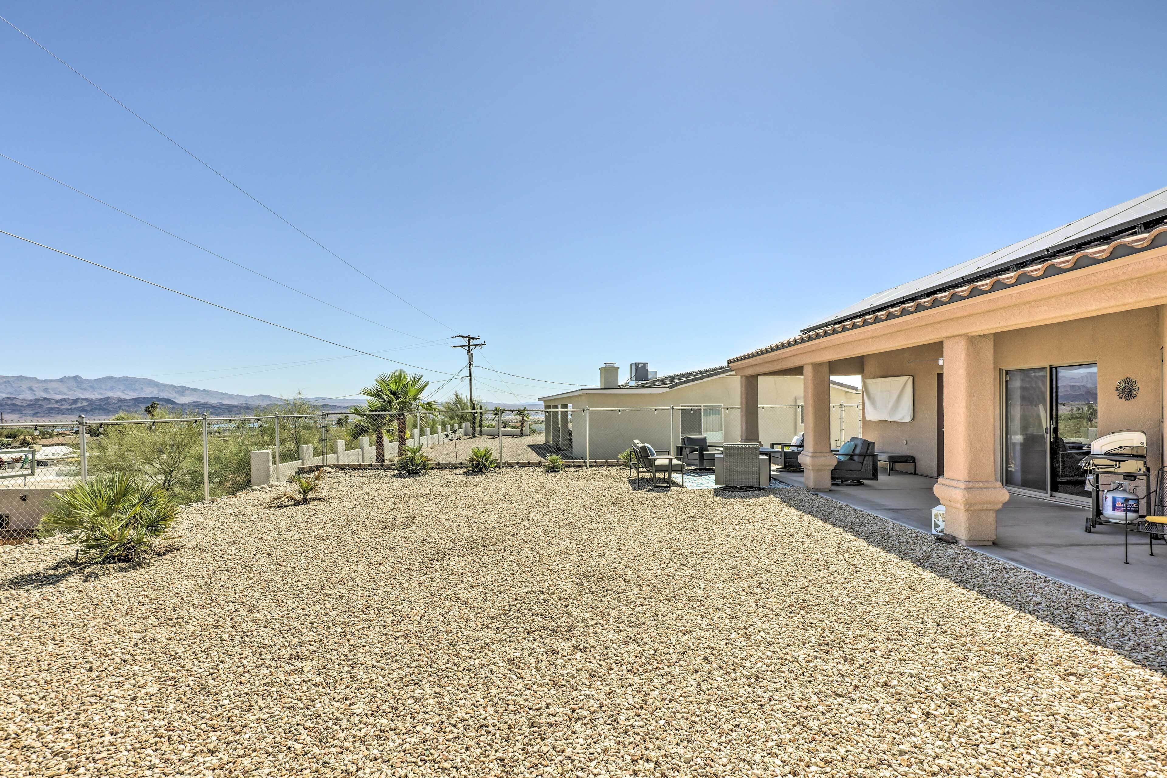 A covered patio area with outdoor seating, a gravel ground, and a view of mountains in the background.