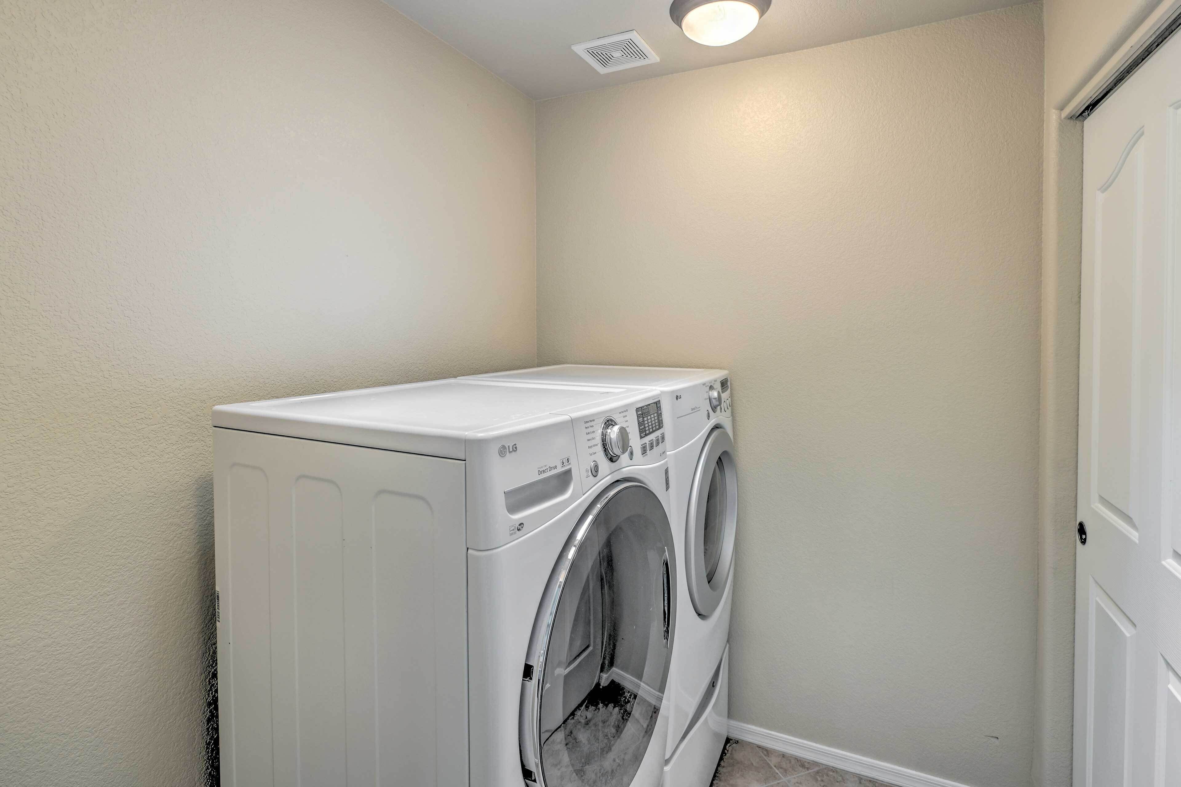 A laundry room with a front-loading washer and dryer, a door, and a ceiling vent.