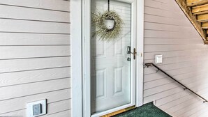 A white front door with a wreath, a light fixture above, and a wooden staircase to the right. - Myrtlewood Golf Resort Condo With Pool Access (Myrtle Beach)