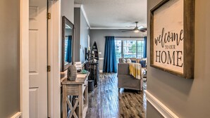 A hallway leading to a living area with a 'Welcome to our HOME' sign, a ceiling fan, and a view of the outside. - Myrtlewood Golf Resort Condo With Pool Access (Myrtle Beach)