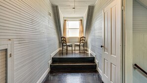 A narrow hallway with wooden paneling, a set of dark wooden stairs, and two wooden chairs facing a window with curtains. - Decatur Farmhouse Getaway w/ Deck & Backyard (Decatur)