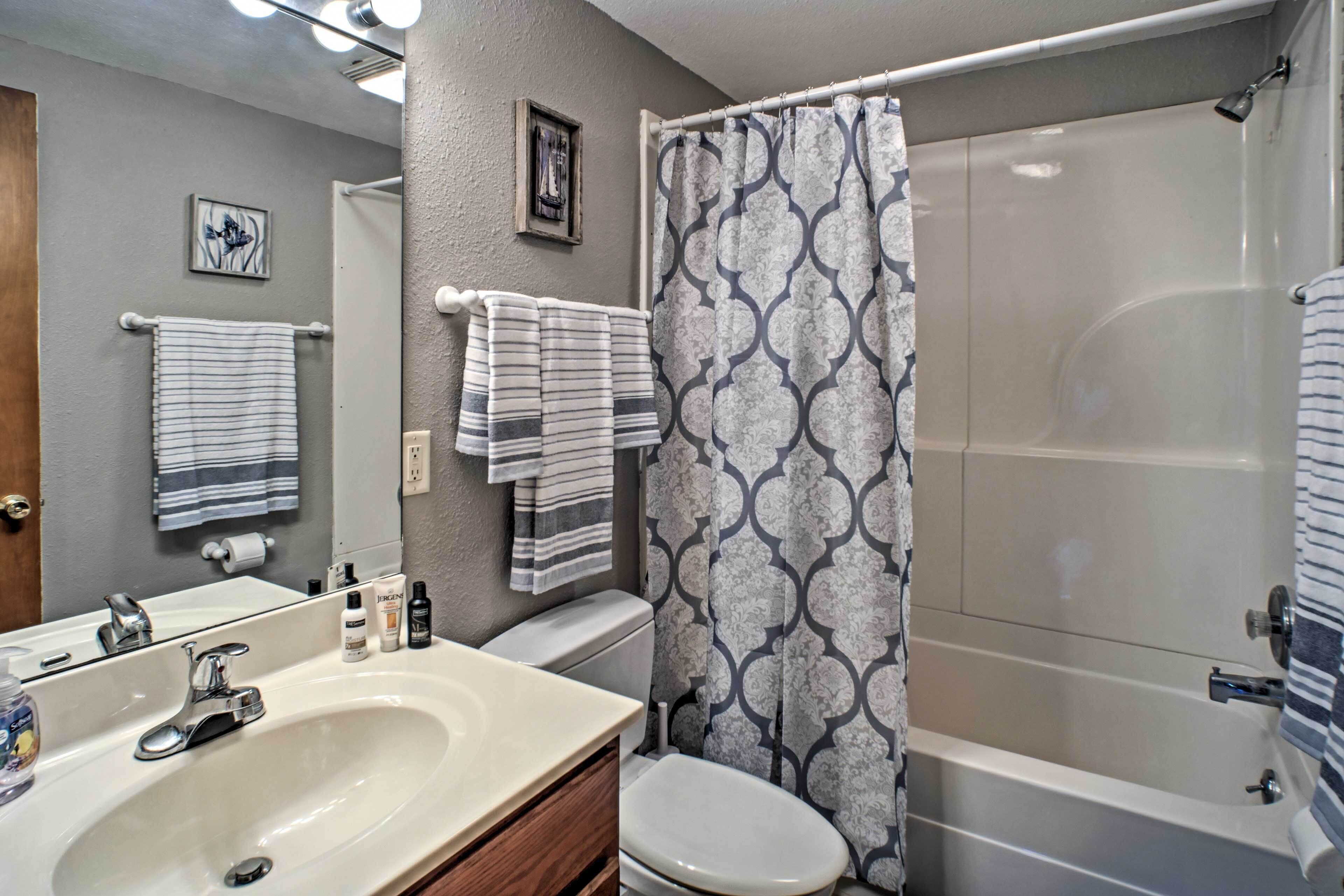 A bathroom with a white sink, toilet, and bathtub. There are striped towels on the towel rack and a shower curtain with a geometric pattern.