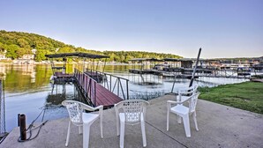 A lakeside patio with white plastic chairs and a wooden deck overlooking a marina with boats and docks. - Boat Dock, Game Room: Lakefront Sunrise Beach Home (Sunrise Beach)