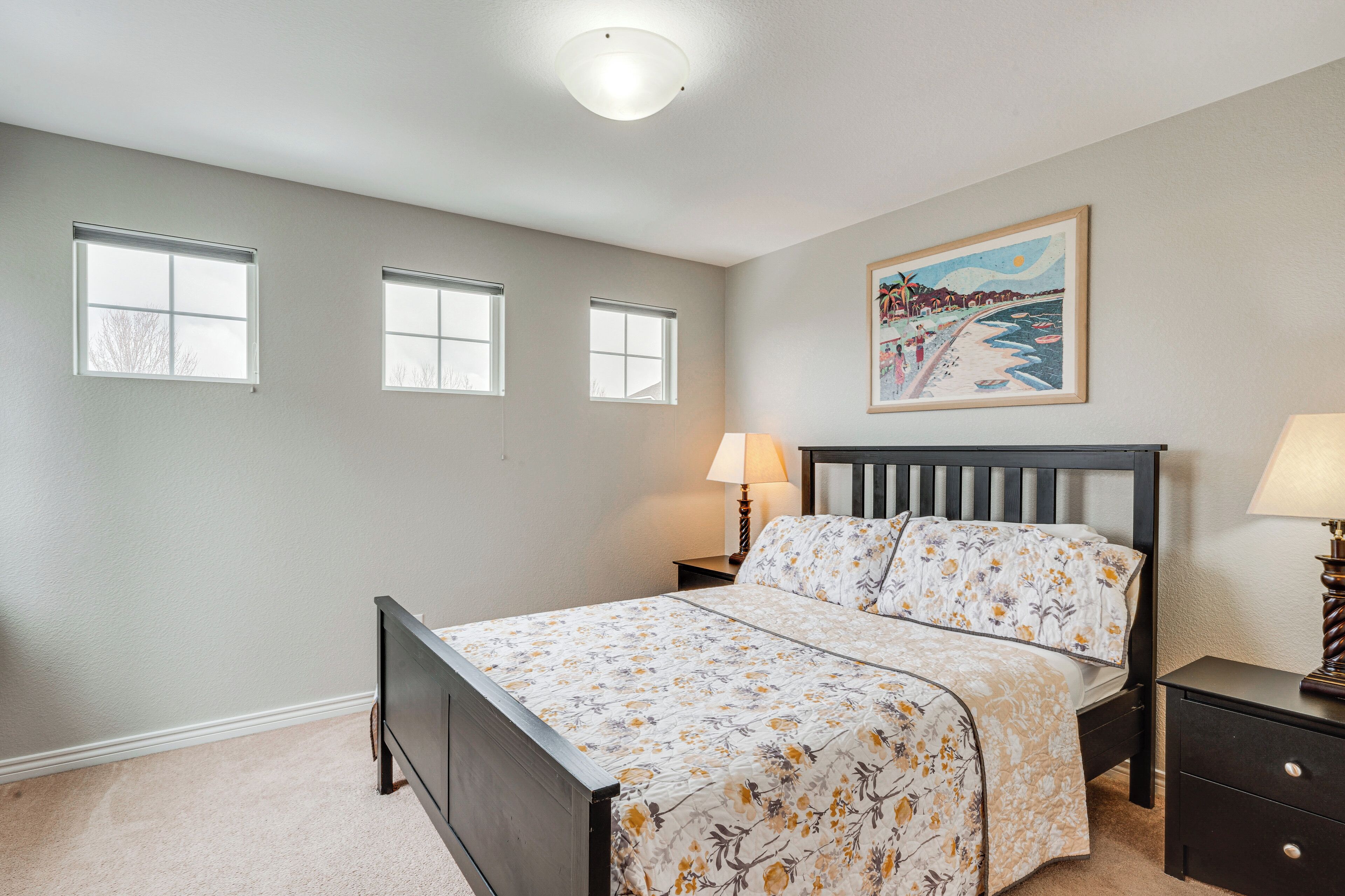A bedroom with a bed, two bedside tables, a nightstand, and a painting on the wall.