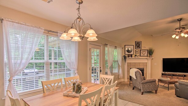 A dining area with a wooden table and white chairs, a fireplace, a television, and a ceiling fan. - Bella Vista Home: Steps to Mountain Biking Trails! (Bella Vista)