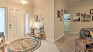 A spacious living room with a leather sofa, a coffee table, and a rug. There is a door leading to another room, and a hallway with a carpeted floor. - Bella Vista Home: Steps to Mountain Biking Trails! (Bella Vista)