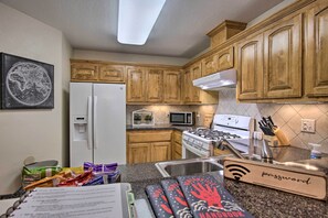 Una cocina con armarios de madera, refrigerador, microondas, estufa y pileta.