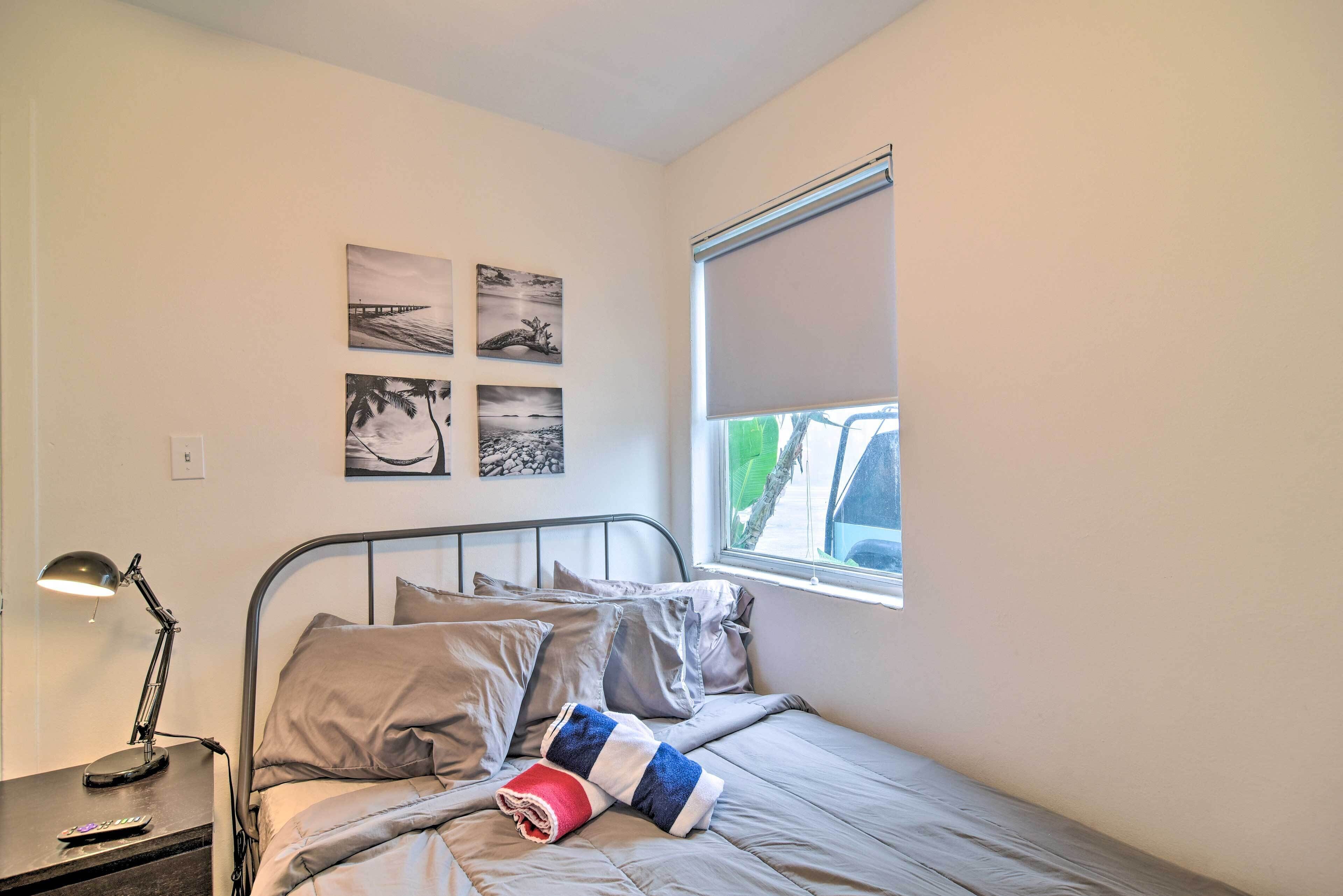 A bedroom with a bed, a nightstand, a lamp, and a window with a blind.