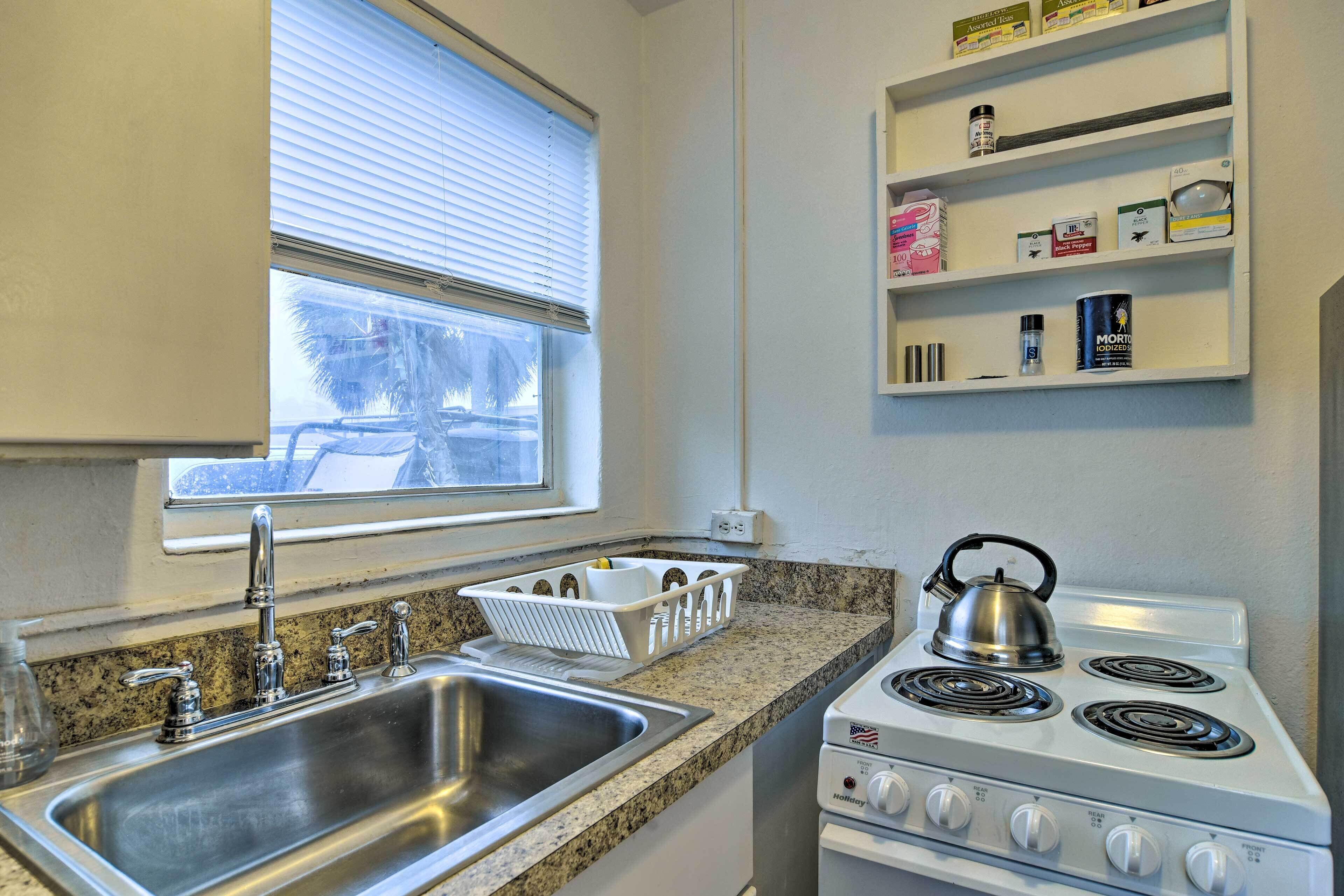 A kitchen with a stainless steel sink, a stove, and a window with blinds.