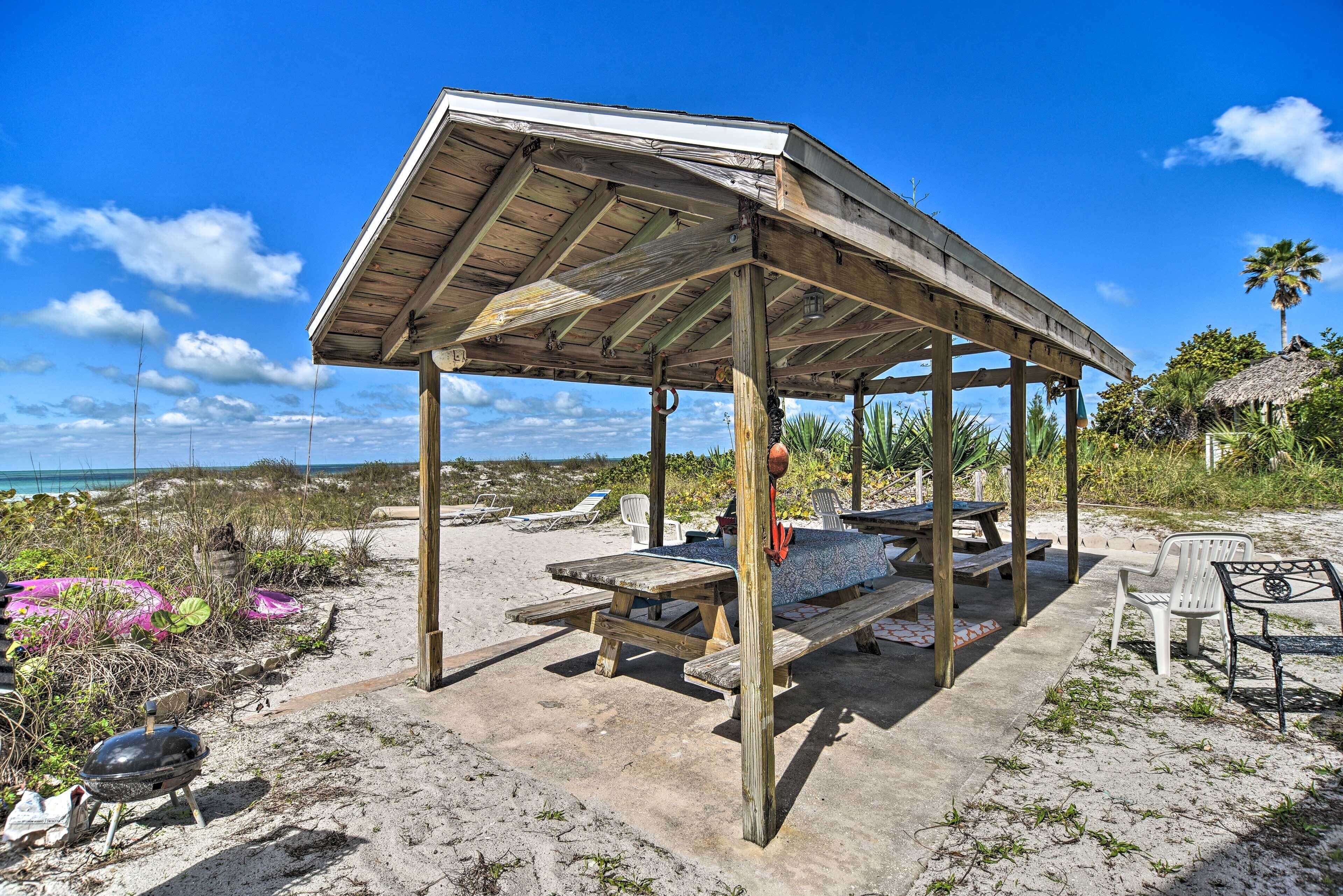 A beachside wooden structure with picnic tables and benches, overlooking the ocean.
