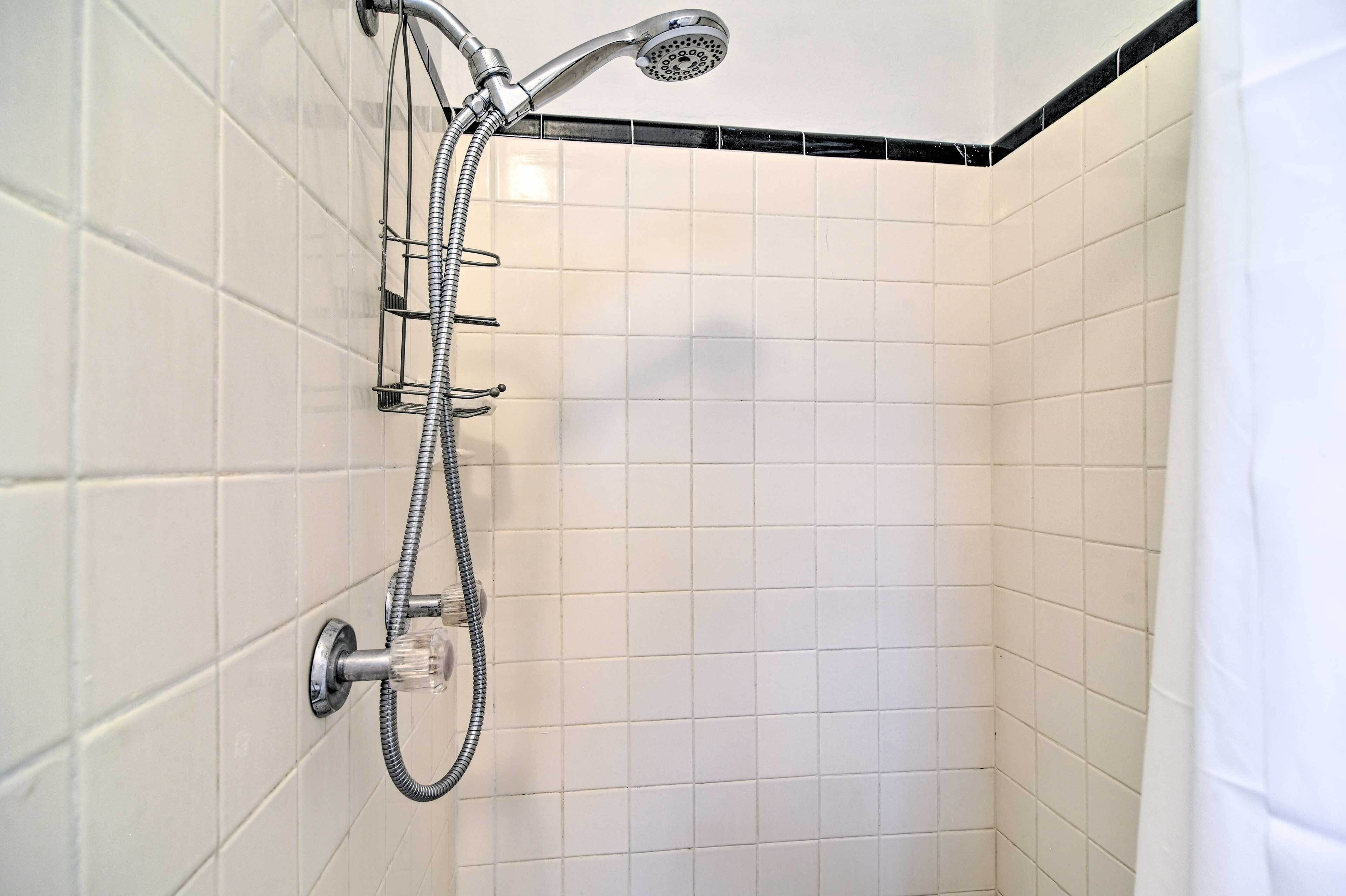 A shower with a handheld showerhead and a fixed wall-mounted showerhead, both with hoses.