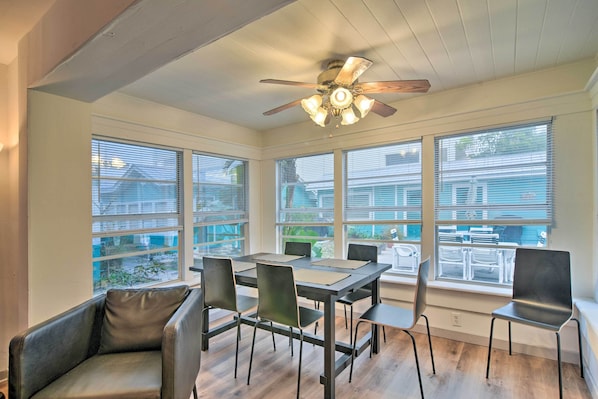 A dining area with a table and chairs, large windows, and a ceiling fan.