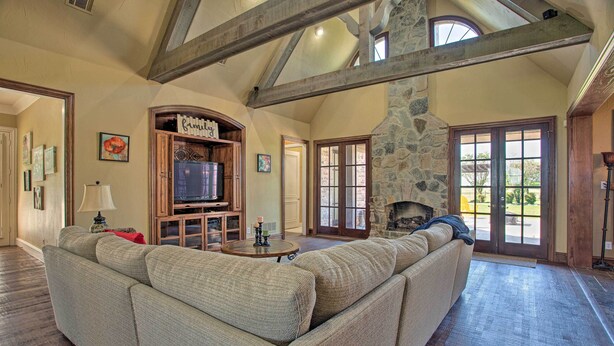 A spacious living room with a large sectional sofa, a stone fireplace, and a stone wall. - Families Welcome! Lavish Celina Home w/ Game Room (Celina)