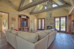 A spacious living room with a large sectional sofa, a stone fireplace, and a stone wall. - Families Welcome! Lavish Celina Home w/ Game Room (Celina)