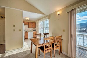 A dining area with a wooden table and chairs, a kitchen in the background, and a view of a snowy landscape through large windows. - Condo w/ Loft: 2 Mi to Windham Mountain Ski! (Windham)