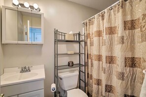 A bathroom with a white sink, a toilet, a mirror with lights, and a shower curtain with a patterned design. - Condo w/ Loft: 2 Mi to Windham Mountain Ski! (Windham)