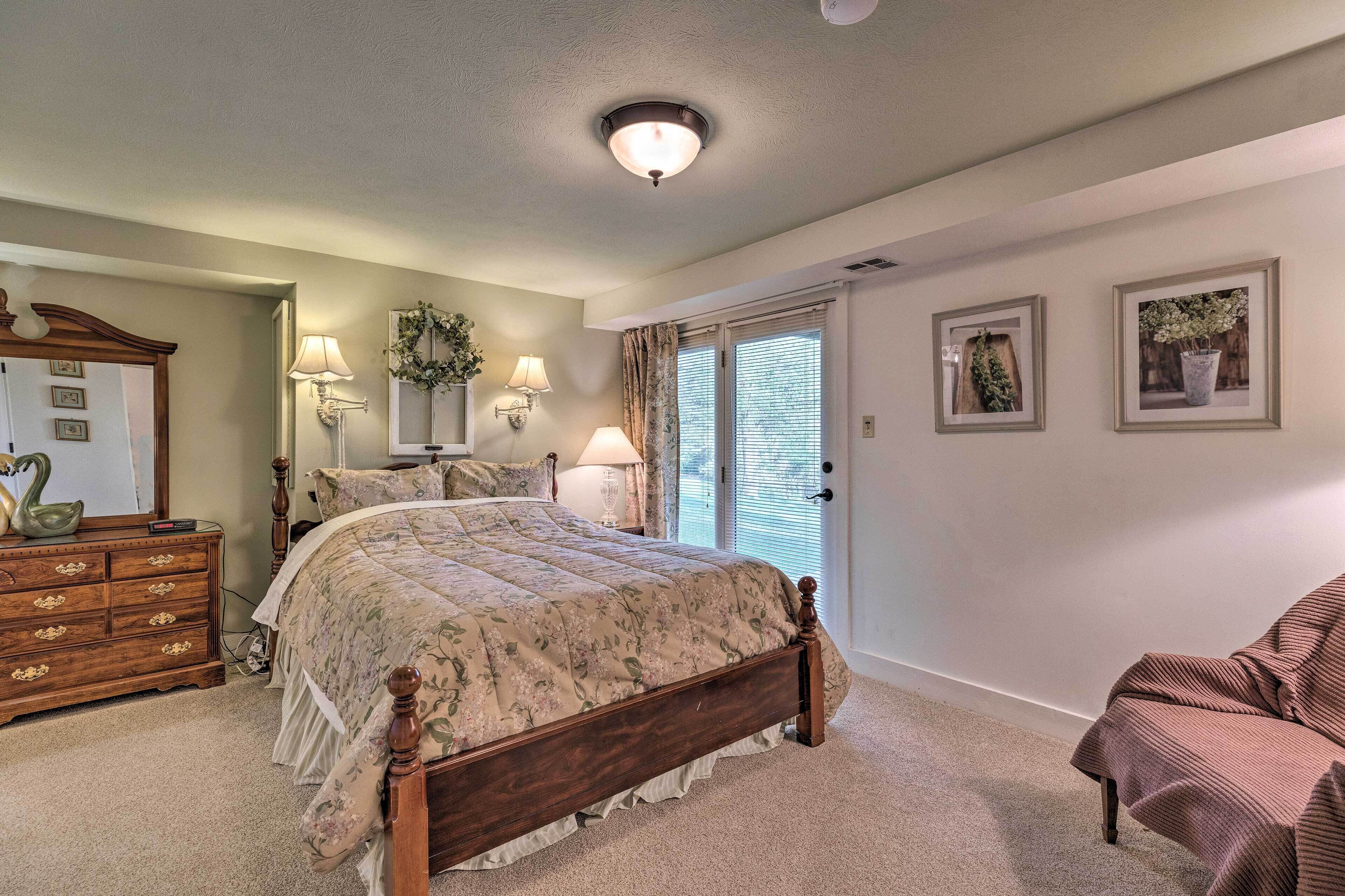 A bedroom with a wooden bed, dresser, and chair. There is a window with curtains and a door with a glass panel.
