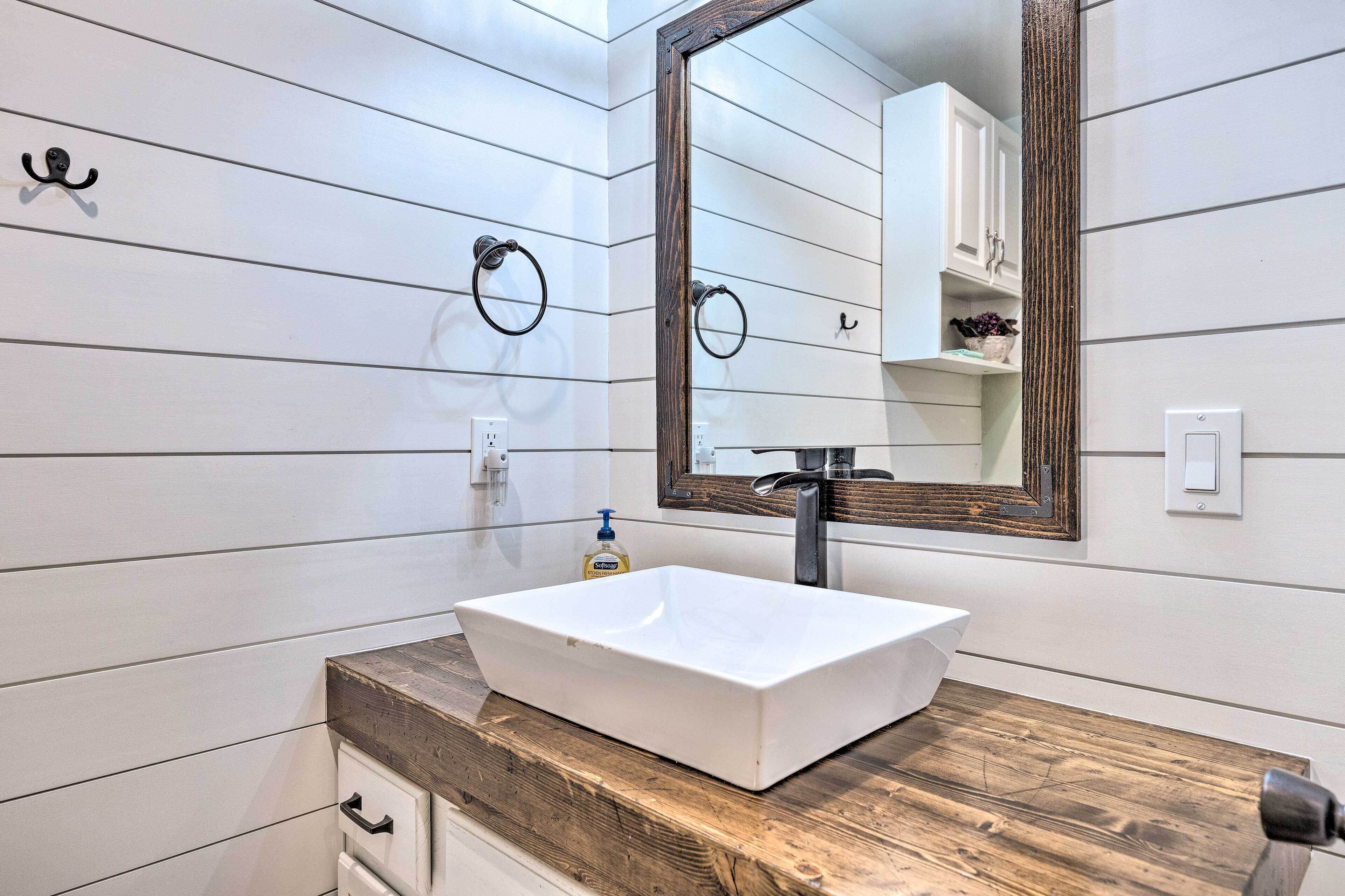 A bathroom with a white vessel sink, wooden countertop, and a large mirror with a wooden frame.