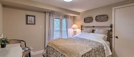 A bedroom with a bed, a chair, a bedside table, a lamp, and a door.