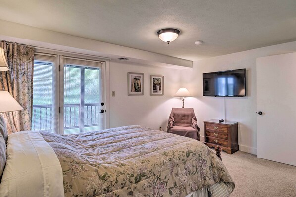 A bedroom with a bed, a chair, a dresser, a TV, and a door.
